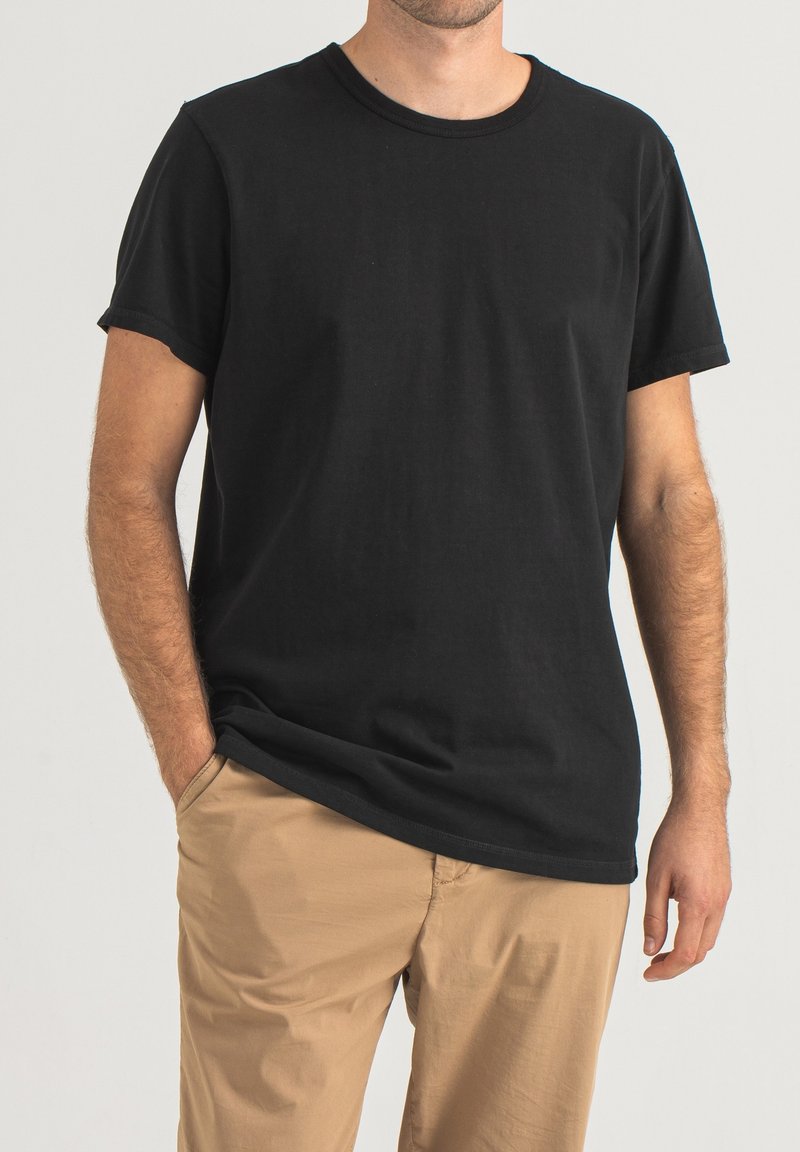 Schwarzes T-Shirt mit kurzen Ärmeln aus Baumwolle; verfügt über einen Rundhalsausschnitt, einen lässigen Schnitt und eine dezente Textur. Kombiniert mit beigen Hosen.