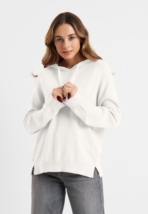 Witte hoodie met een gestructureerde afwerking, voorzien van een trekkoordkap en roze accenten bij de mouwmanchetten. Geraadpleegd met grijze spijkerbroek.