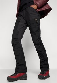 Black outdoor pants with a tapered fit, featuring zippered and buttoned pockets, textured fabric, and reinforced knee panels.