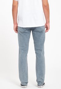 Jeans de mezclilla azul claro con corte recto, costuras en contraste y dos bolsillos traseros. Llevados con una camiseta blanca y zapatillas negras.