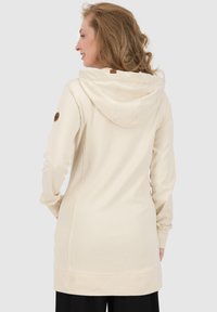 Helle beige Kapuzenjacke mit Kängurutasche, geripptem Saum und Stoffetikett am Nacken. Weiche Textur und lange Ärmel.