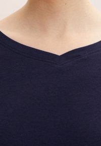 Námořnická modrá pánská V-krční tričko vyrobené z jemné bavlny, s hladkou texturou a jednoduchým, čistým designem výstřihu.