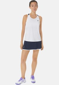 Witte sportieve tanktop met marineblauwe bies, gecombineerd met een marineblauwe rok. Bevat vochtafvoerende stof en een aansluitend ontwerp voor optimale prestaties.