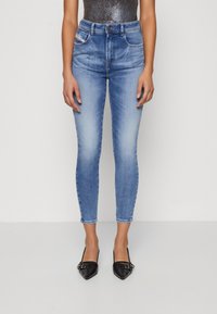 Vaqueros ajustados de color azul con un lavado desgastado, cintura alta y cinco bolsillos, combinados con tacones negros de punta afilada con detalles de hebilla.