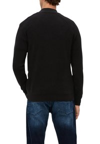 Schwarzer gerippter Strickpullover mit rundem Halsausschnitt und langen Ärmeln, mit einer einfarbigen Textur und klassischem Design. Getragen mit blauen Jeans.