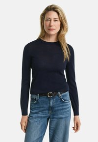 Marineblaues Langarmoberteil aus leichtem Material, kombiniert mit hoch taillierten hellblauen Jeans und einem schwarzen Gürtel.