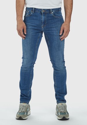 Jeans in denim azzurro chiaro con vestibilità slim, design a cinque tasche e cuciture sottili. Abbinati a sneakers grigie e verdi.