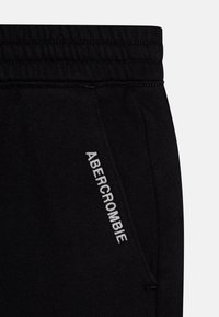 Zwarte sweatpants met een elastische tailleband, zijzakken en witte geborduurde "ABERCROMBIE" tekst langs de zijnnaad. Zachte stof kwaliteit.