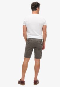 Pantalones cortos de algodón grises con bolsillos traseros y botones marrones, combinados con una camiseta blanca lisa y zapatos náuticos marrones.