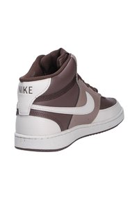Sneaker alte con tomaia in pelle marrone e beige, dettagli bianchi, collare testurizzato e logo Nike ben in vista sul tallone.