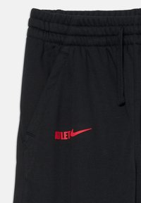 Crne atletske hlače s elastičnim pojasom, bočnim džepom i crvenim logom "ATLET" s crvenim Nike znakom sprijeda. Mekana tekstura tkanine.