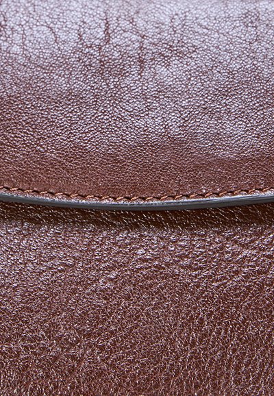Surface en cuir brun texturé avec des surpiqûres détaillées le long d’un bord courbé, montrant le grain naturel et un léger éclat.