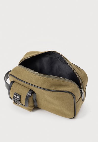 Συμπαγής τσαντάκι για είδη προσωπικής υγιεινής από καμβά σε ελιά πράσινο χρώμα με μαύρη επένδυση, ανοιχτό φερμουάρ και μπροστινή τσέπη με κούμπωμα και μεταλλικό κρίκο.