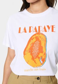 Valge puuvillane T-särk, millel on oranž ja kollane papaya graafika kirjutisega "LA PAPAYE" ja "marche aux fruits" ning täpimustriga.