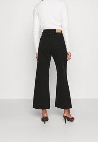 Schwarz weit geschnittene Jeans aus Denim mit hoher Taille, unsichtbaren Gesäßtaschen und einem beige Markenetikett am Bund.
