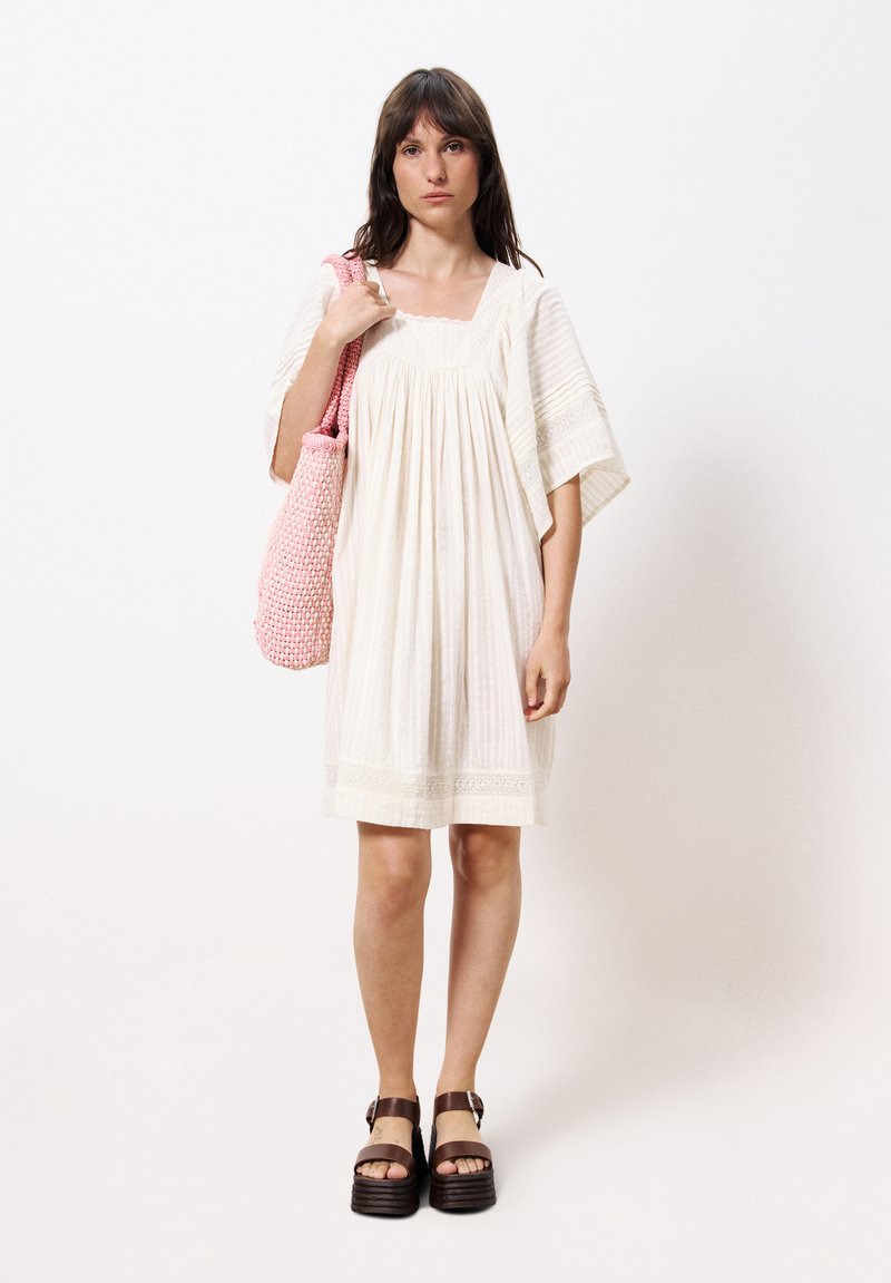 Weißes, locker sitzendes Kleid mit strukturierten Streifen und Spitzenakzenten, kombiniert mit einer rosa geflochtenen Tasche. Braune Plattformsandalen. Einfaches, lässiges Design.