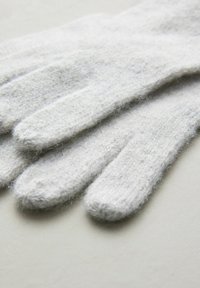 Witte, zacht-textuur handschoenen liggen plat op een lichte ondergrond, met zichtbare vingercompartimenten en een gezellige, gebreide uitstraling.