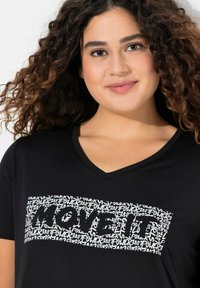 Zwarte V-hals t-shirt met een grote grafische print met herhalende tekst "POWER" en "MOVE IT" in het wit, die sterk typografie benadrukt op een zachte stof.