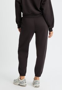 Pantalones de chándal negros de algodón con puños elásticos, que presentan un corte holgado. Se llevan con zapatos deportivos grises, mostrando una textura suave.