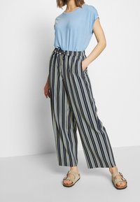Jasnoniebieska koszulka zestawiona z granatowymi i kremowymi spodniami w szerokie paski, posiadającymi elastyczny pas i boczne kieszenie. Uzupełniona beżowymi sandałami.