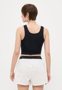 Svart linne med en skräddarsydd design och breda axelband, parat med vita shorts som har ett svart midjeband med en flerfärgad "Calvin Klein"-etikett.