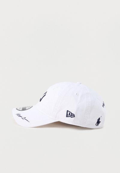 Λευκό καπέλο μπέιζμπολ με μαύρα κεντημένα λογότυπα και κείμενο, συμπεριλαμβανομένου ενός εμβλήματος με άλογο και αναβάτη και στυλιζαρισμένα γράμματα στις πλευρές και τη γείσο.