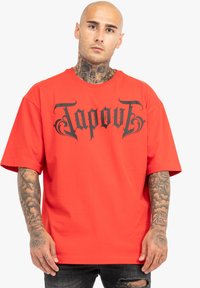Sarkanais īsās piedurknes T-kreklis, kas izgatavots no kokvilnas, ar lielu melnu "Tapout" logo priekšā. Piegriezums ir brīvs, ar apļa kaklu.