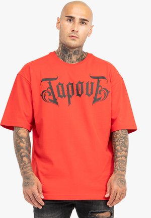 Rød kortærmet T-shirt lavet af bomuld, med et stort sort "Tapout" logo over fronten. Den har en løs pasform med en rund hals.