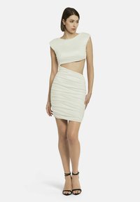 Witte bodycon jurk met kapmouwen, uitsnijding in het midden en gerimpelde textuur. Gekleed met zwarte strappy hakken.