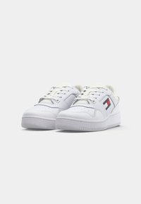 Paire de baskets basses blanches avec lacets et un petit logo Tommy Hilfiger rouge, blanc et bleu sur les côtés.