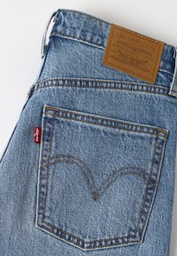 Πίσω τσέπη μπλε τζιν Levi's με χαρακτηριστική ραφή, κόκκινη ετικέτα Levi's και καφέ δερμάτινη ετικέτα μάρκας στη μέση.