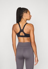 Zwarte sportbeha met verstelbare bandjes en een keyhole-ontwerp, gecombineerd met hooggetailleerde grijze leggings. Soepele textuur en strakke pasvorm.