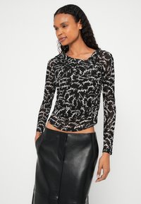 Mustast pikast varrukast pluus kõrge kaelusega, millel on läbipaistev kangas ja valge käsitsi kirjutatud tekstimuster; kombineeritud musta nahast seelikuga.