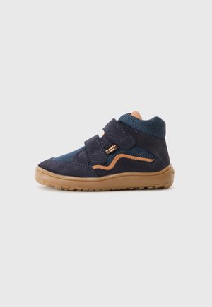 Chaussure pour tout-petit bleu marine avec semelle marron, deux bandes velcro et une bande d’accent orange sur un fond gris clair uni.