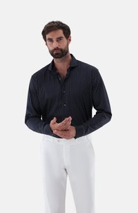 Gestreiftes langärmliges Shirt in Marineblau und Weiß aus leichtem Stoff, kombiniert mit weißen Hosen. Es hat einen Kragen und eine durchgehende Knopfleiste.