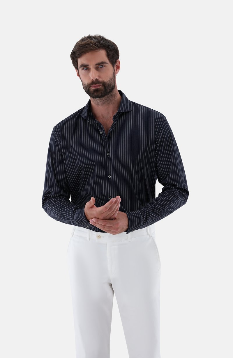 Gestreiftes langärmliges Shirt in Marineblau und Weiß aus leichtem Stoff, kombiniert mit weißen Hosen. Es hat einen Kragen und eine durchgehende Knopfleiste.