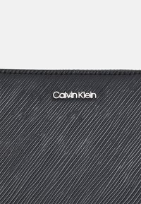 Portafoglio nero dalla texture a righe verticali, con il logo argentato "Calvin Klein" sul fronte. Il materiale ha una finitura liscia.