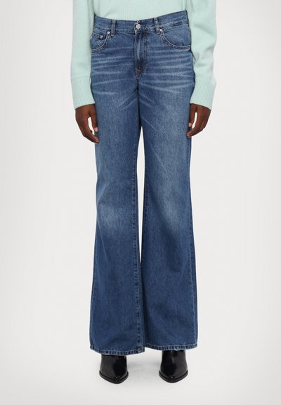 Udsvingende jeans i blå denim med en faded vask, som har fem lommer og sølv knappestik, parret med en lys sweater og sorte støvler.