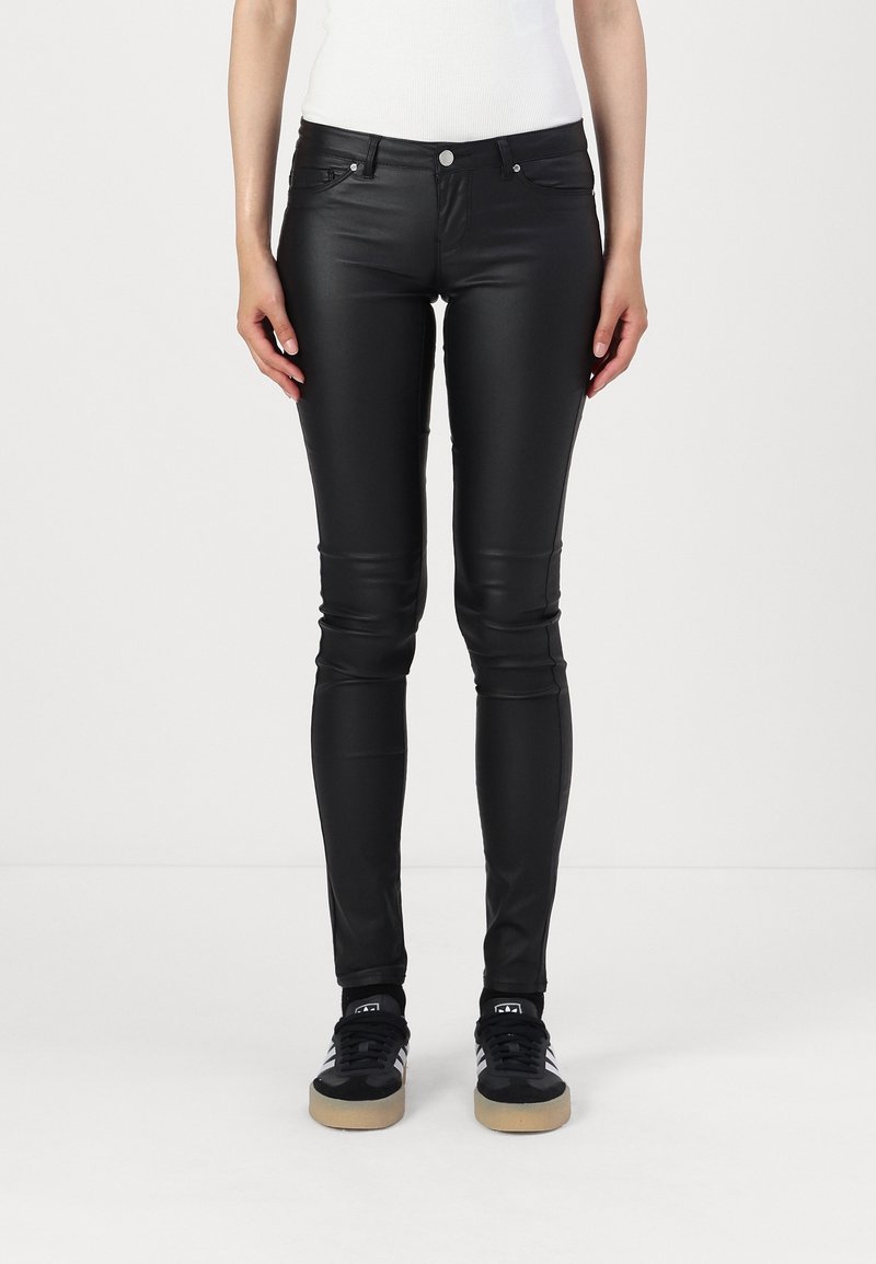 Pantalones ajustados de imitación cuero negros con una textura suave, diseño ceñido y estilo clásico de cinco bolsillos, combinados con zapatillas negras.