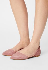 Flats à bout pointu en daim rose pâle, dotées d'un petit talon et d'un design ajouré, mettant en valeur une texture lisse avec un panneau supérieur contrastant.