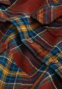 Chemise en flanelle à carreaux rouges et bleus avec des accents jaunes et blancs. Dotée de boutons marron et d'une texture brossée pour plus de chaleur.