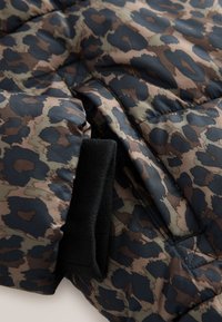 Veste matelassée avec un motif léopard dans des tons terreux de brun, noir et vert profond ; comprend un poignet noir texturé.