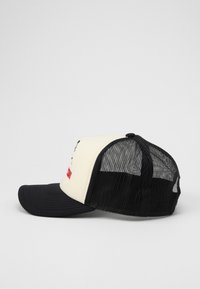 Cappello da camionista con pannello frontale crema, retro in rete nera, visiera curva nera e grafica stampata con testo rosso.