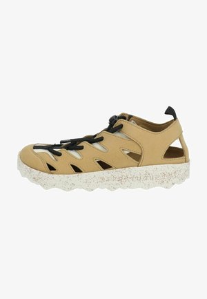 Light tan sneaker with cut-out design, black laces, and a textured white speckled sole. Features a soft suede material and open heel.