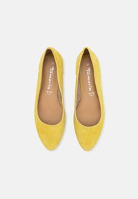 Paire de chaussures plates en daim jaune à bout pointu avec semelles intérieures marron étiquetées Tamaris taille 37 sur fond blanc.