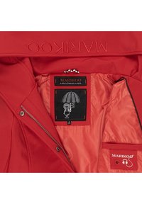 Chaqueta roja con exterior liso, forro interior, múltiples bolsillos, nombre de la marca bordado y una etiqueta gráfica divertida.