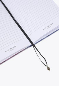 Carnet à couverture rigide avec des pages lignées, doté d'un marque-page ruban noir et d'un pendentif décoratif en forme de feuille. La couverture présente un dégradé de couleurs violet et bleu.