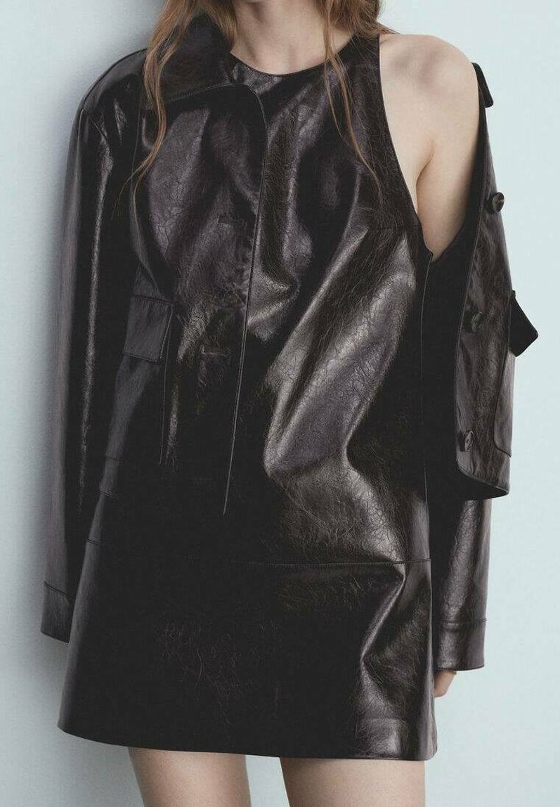 Personne portant une robe asymétrique en cuir noir avec une épaule découverte et une manche longue de l'autre côté.