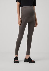 Leggings de maternidade em castanho escuro, com cintura alta, tecido macio e elástico, textura suave e design justo. Combinados com sandálias de plataforma pretas.