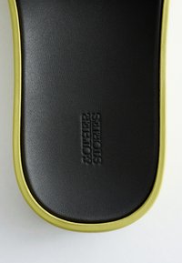 Semelle de sandale noire et verte avec surface texturée et texte embossé « SOFTER SHOES » centré sur la zone noire sur fond blanc.